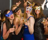 Attractive women wearing masks holding champagne looking at camera